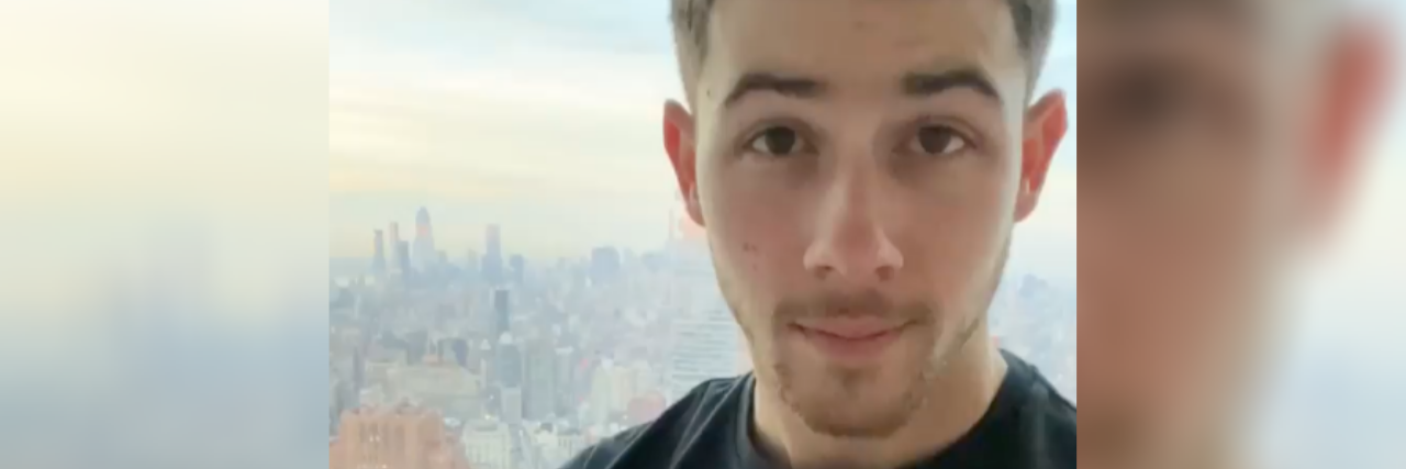 Nick Jonas Launches Initiative to Increase Access to Insulin Nick Jonas standing in front of a window that shows a hazy city skyline