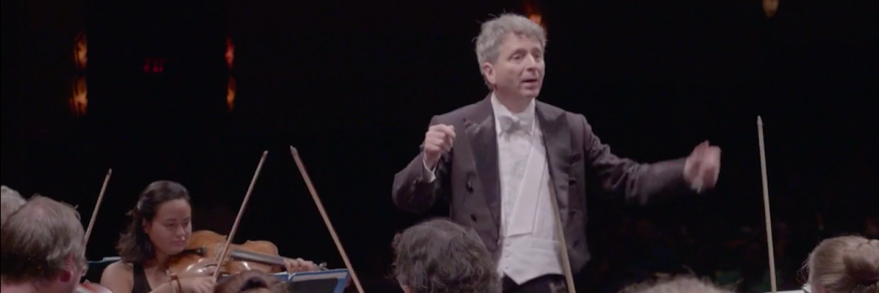 Conductor Ronald Braunstein wears a formal tux while directing an orchestra
