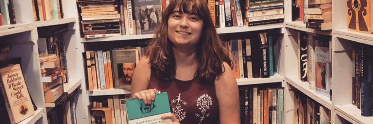 Would I Be a Different Person if I Didn't Have Mental Illness? photo of the contributor surrounded by bookshelves and holding a book on creative writing