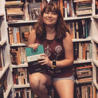 photo of the contributor surrounded by bookshelves and holding a book on creative writing