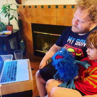 Benny attending Zoom kindergarten with his dad sitting beside him.