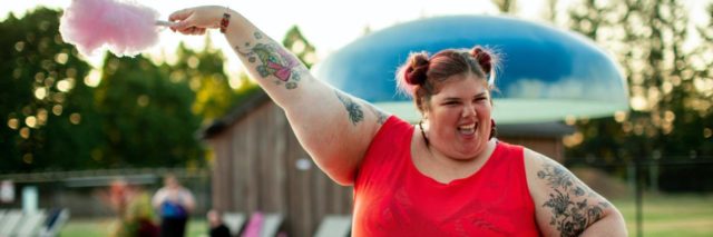 A woman, fat and happy, holding up cotton candy at a pool
