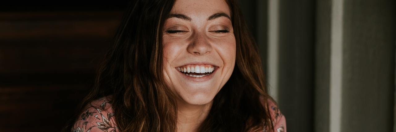 How I Know My Mental Health Is Improving photo of young woman sitting on stairs smiling with eyes closed