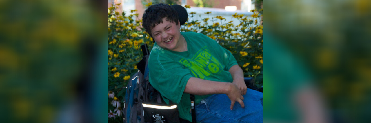 Chelsie smiling as she sits in her power wheelchair outdoors with flowers in the background.