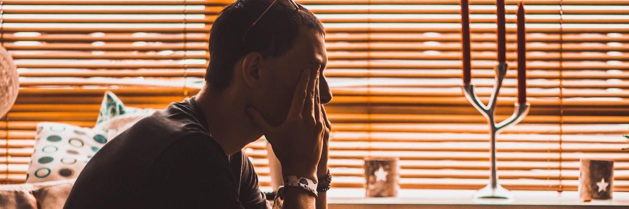 It's Normal to Have Sexual Feelings for Your Therapist (But They Should Never Have Sex With You) Profile of a man sitting on a couch with his head in his heads, rubbing his eyes in distress