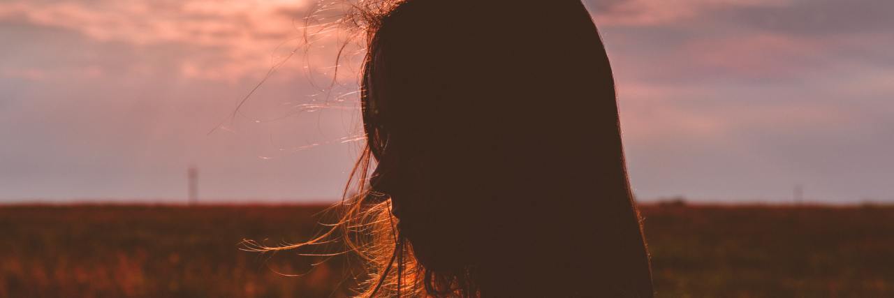 I'm Turning to Drinking Again as My Mental Health Gets Worse woman with dark hair standing sideways to the camera in a field of flowers looking down