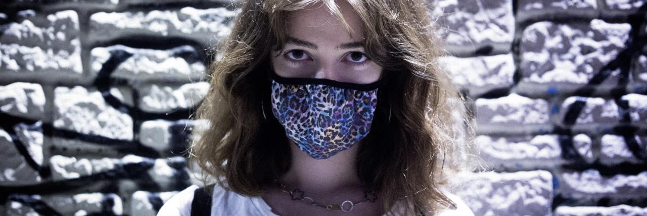 Struggling With People Not Caring About COVID-19 and the Future photo of woman wearing a colorful face mask and looking into camera, standing against brick wall