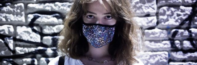 photo of woman wearing a colorful face mask and looking into camera, standing against brick wall