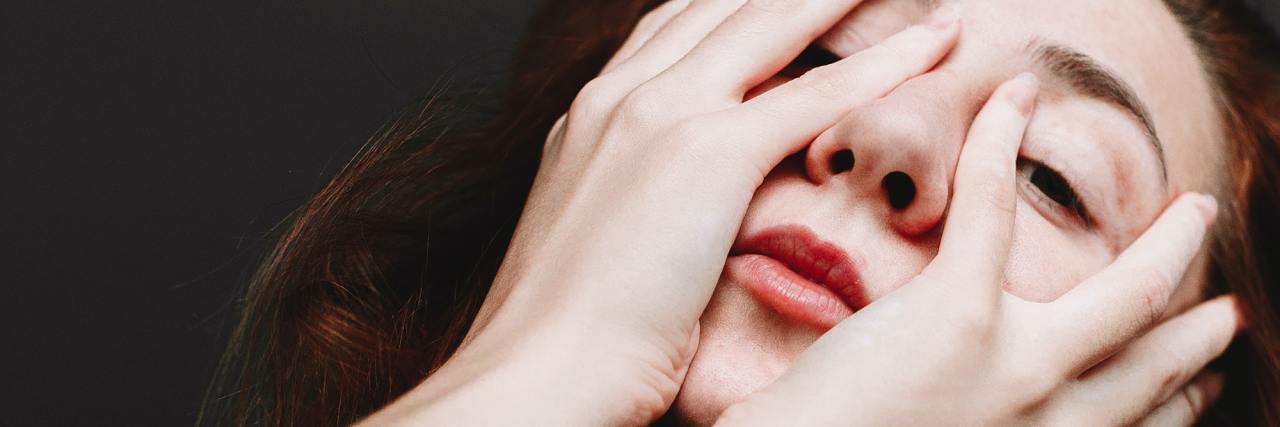Mental Illness Symptoms That Make You Feel Ashamed and Guilty photo of young woman partially covering her face with hands but looking at camera