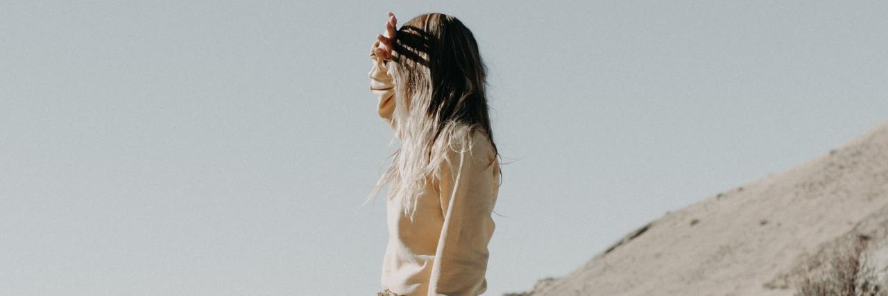 photo of young woman standing on rocky slope looking at sunset