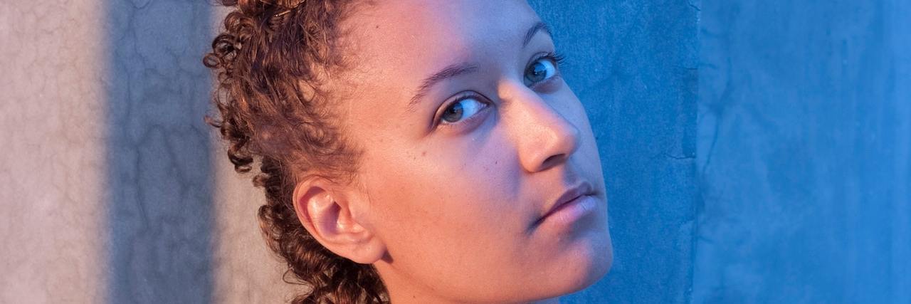 Can You Experience Psychosis With Bipolar Disorder? Woman with short cropped hair looks sideways at the camera against a concrete wall