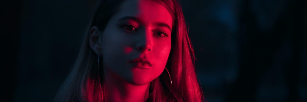 Read This if You Hate Yourself and You Don't Know Why photo of woman looking into camera in red light, looking stern or upset