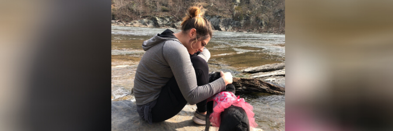 Woman sitting by the banks of a river, petting a dog
