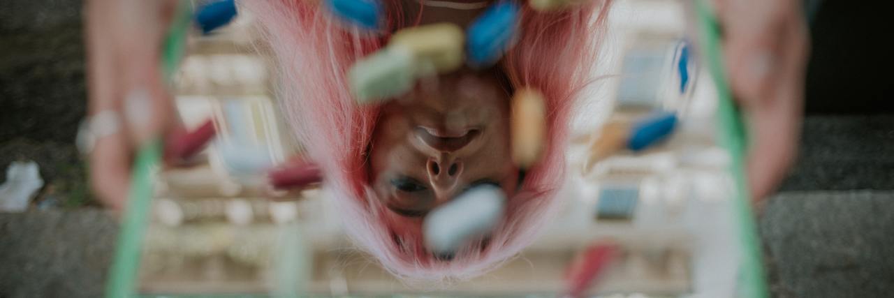 Read This if You're Struggling With an Undiagnosed Mental Illness reflection of a woman with pink hair, with pills resting on the reflection