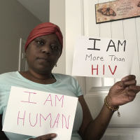 photo of contributor holding two signs, one saying "I am human" and one saying "I am more than HIV"