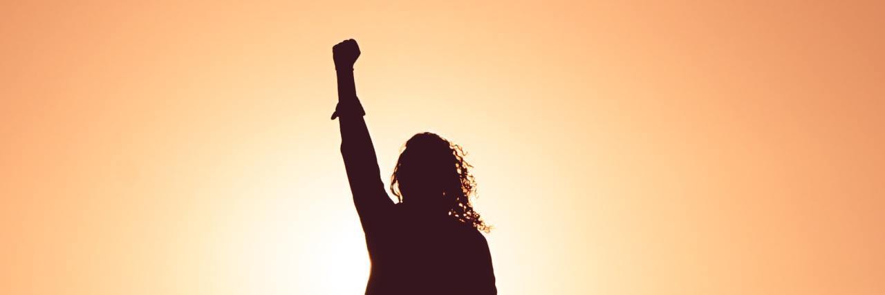 Silhouette of woman with her fist raised in the air.
