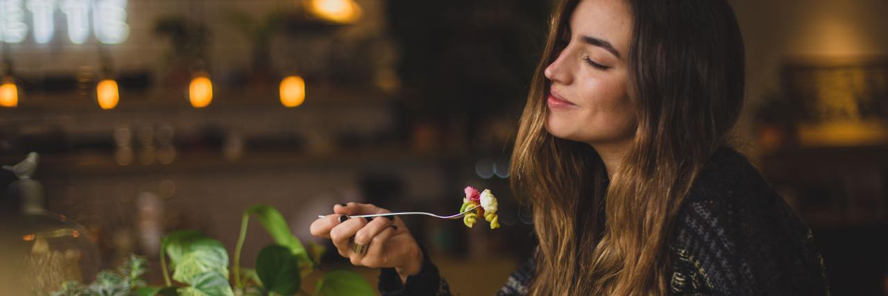 How Food Can Help With Mental Illness and Chronic Illness Recovery photo of woman holding a fork with pasta, eyes closed and smiling