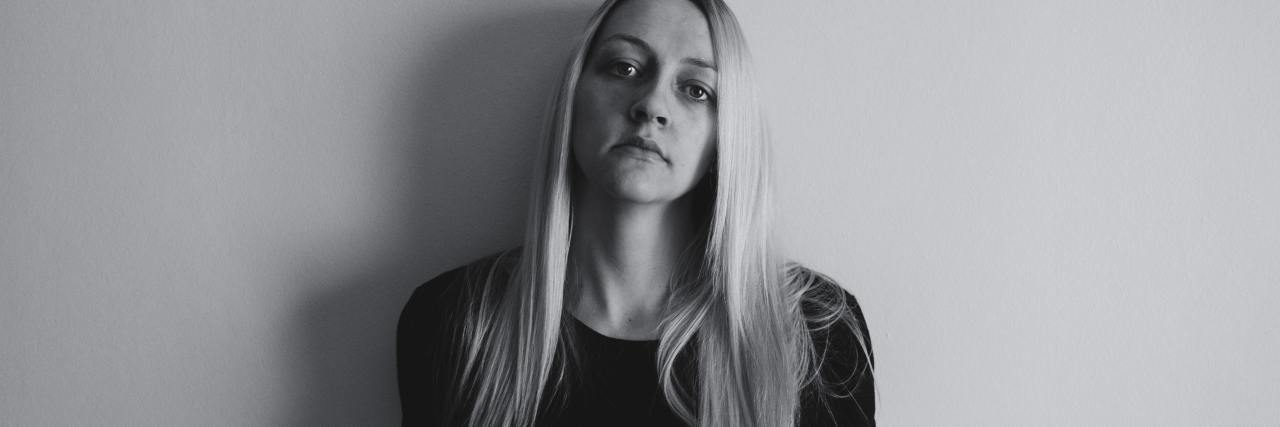 Anxiety Makes Me Feel Like a 'Weird' Person black and white photo of woman standing against plain background and looking into camera with serious expression