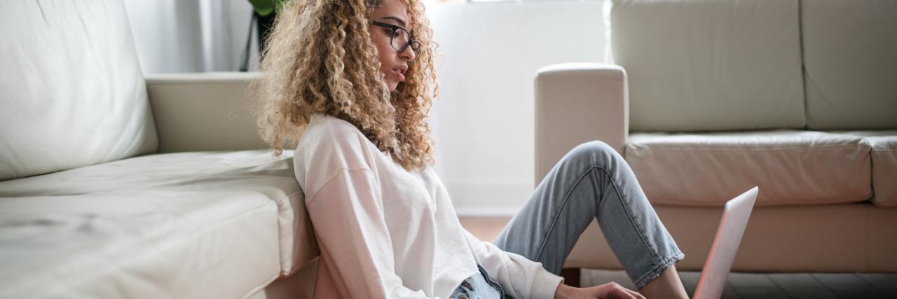 photo of student sitting on floor in front of sofa with a laptop on her knee