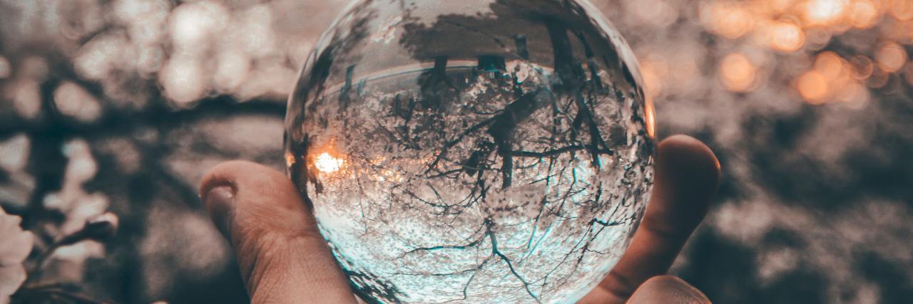 Woman holding crystal ball with trees in background.
