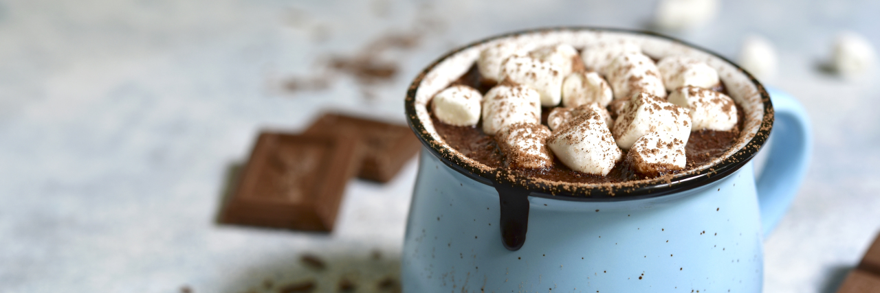 21 Easy (and Cozy) Self-Care Ideas to Practice This Winter Homemade hot chocolate with mini marshmallow in a blue enamel mug on a light slate background.