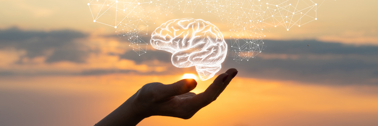 Getting an Auditory Processing Disorder Diagnosis as an Adult Hand holding drawing of brain with sunset background.