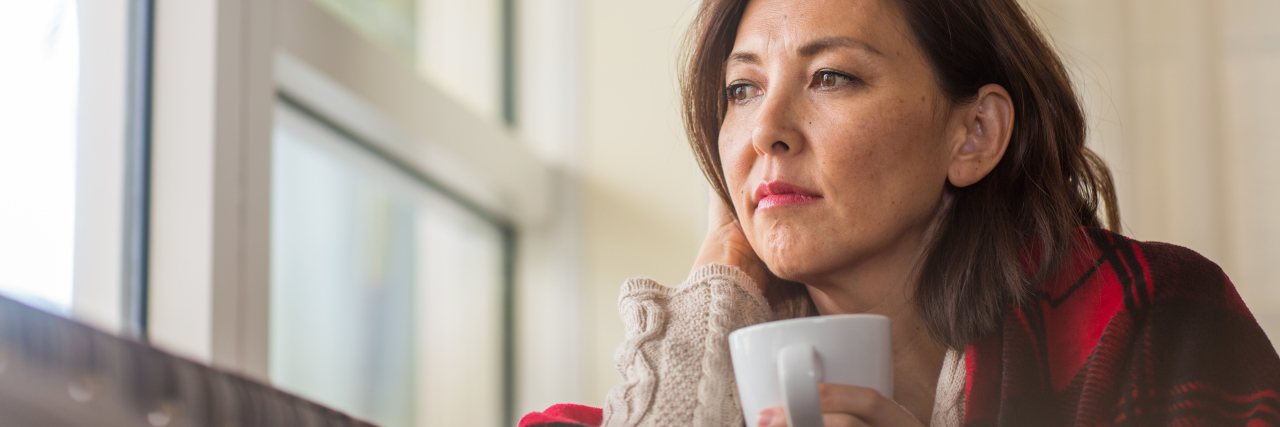 When Holidays Become a Marker of Disease Progression Sad woman looking out the window while drinking coffee.