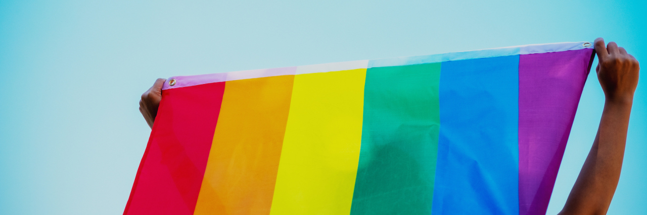 Waiting for U.S. Election Results as a Nonbinary Lesbian People holding and raising a rainbow flag over the blue sky