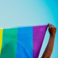 People holding and raising a rainbow flag over the blue sky
