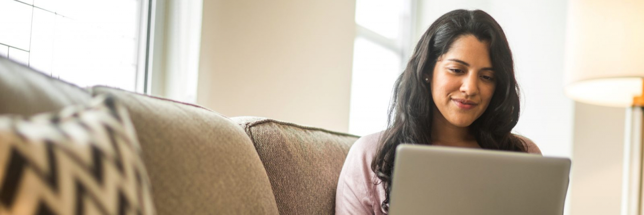 Woman of color smiling while on her laptop on couch