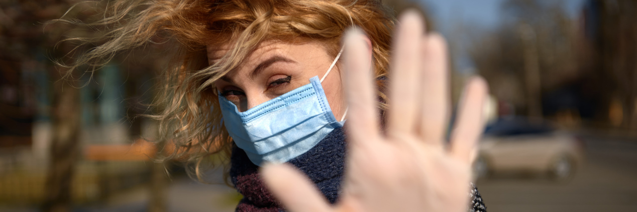woman in a medical mask and rubber gloves raising hand to stay away and keep distance.