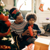 Happy African American mother with kids opening Christmas presents at home.