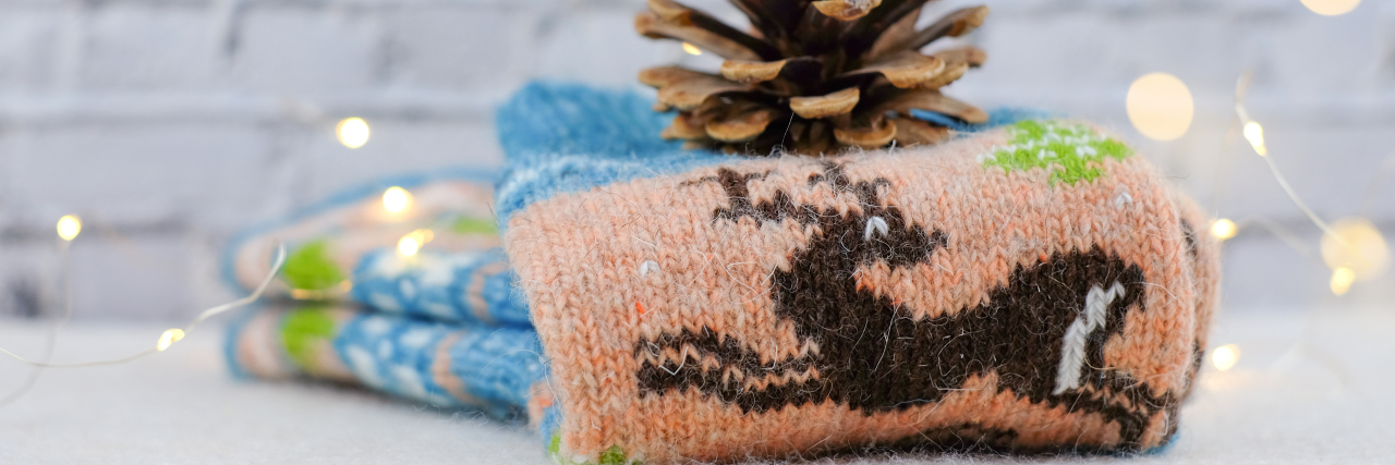 Gift Ideas for Someone Living With More Than One Chronic Illness Christmas socks, pine cone against white brick wall.