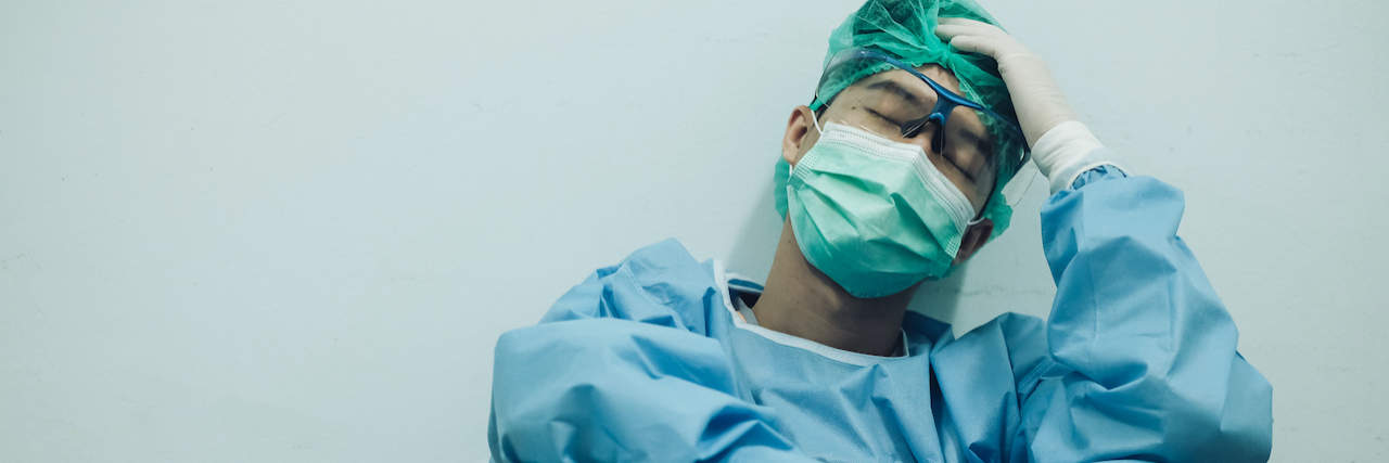 The Pandemic's Dangerous Mental Health Effects on a Frontline Medical Worker Asian medical worker in full PPE sitting and holding head in his hand