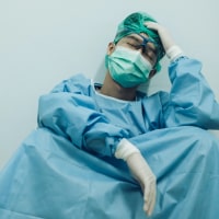 Asian medical worker in full PPE sitting and holding head in his hand