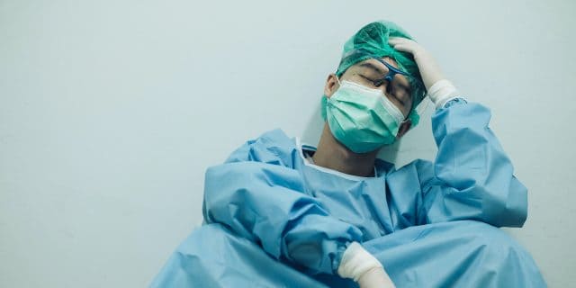 Asian medical worker in full PPE sitting and holding head in his hand
