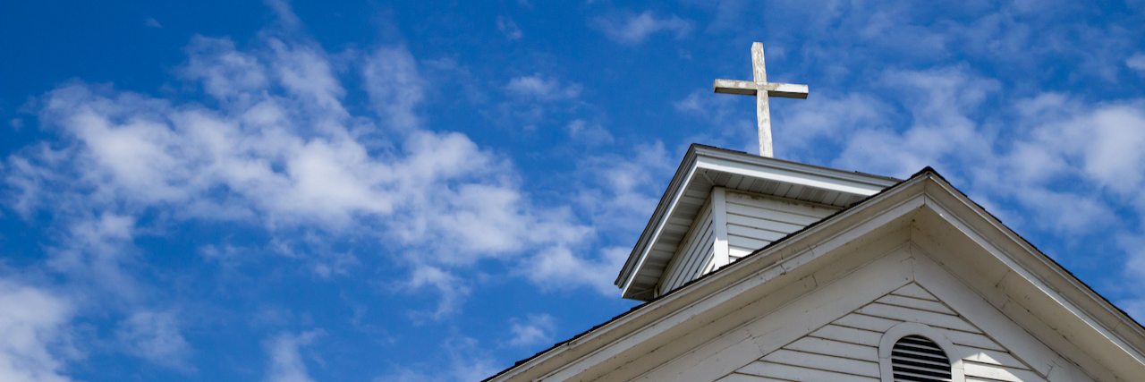Wooden cross on a simple steeple set against a sunny summer blue sky.