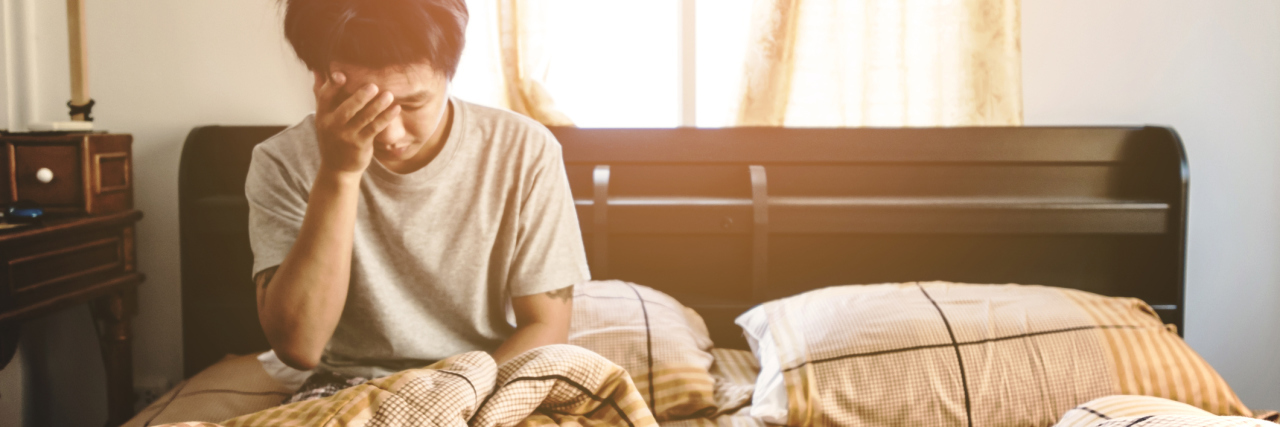 Read This If Depression Feels Beyond Words Right Now photo of man sitting upright in bed alone, looking tired or upset