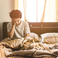 photo of man sitting upright in bed alone, looking tired or upset