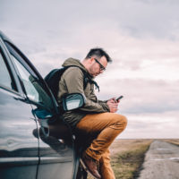 White man sitting on his car, texting someone, on a deserted road