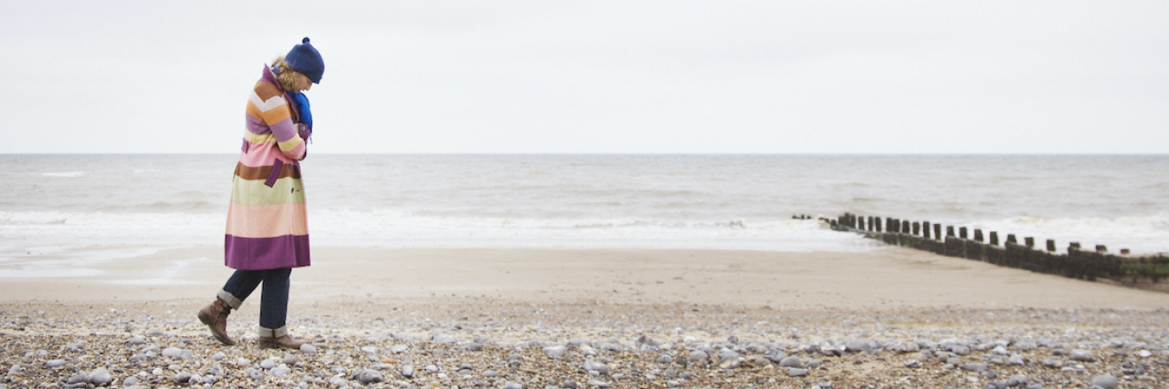 How Depression Takes Away Psychological Safety A woman wearing a heavy winter coat, talking on the beach with her head down