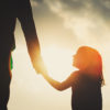 silhouette of a little girl holding a parent's hand during sunset