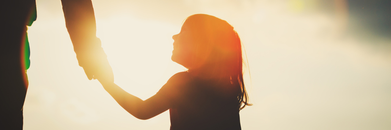 silhouette of a little girl holding a parent's hand during sunset