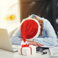 Tired woman wearing Santa hat sleeping at laptop.