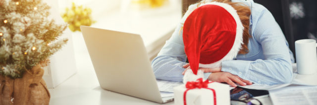 Tired woman wearing Santa hat sleeping at laptop.