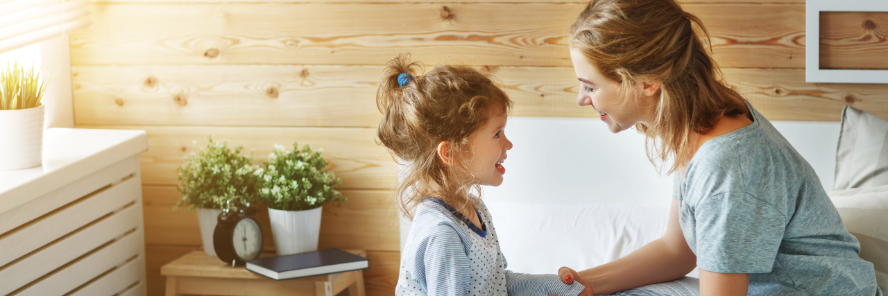 What My Daughter's Speech Therapy Made Me Realize About Mental Health a mom and her young daughter are sitting on a bed smiling at each other and holding hands