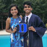 The author and her brother, smiling. He wears a graduation gown and they're both holding his graduation cap. They're standing outside, in front of a pool.