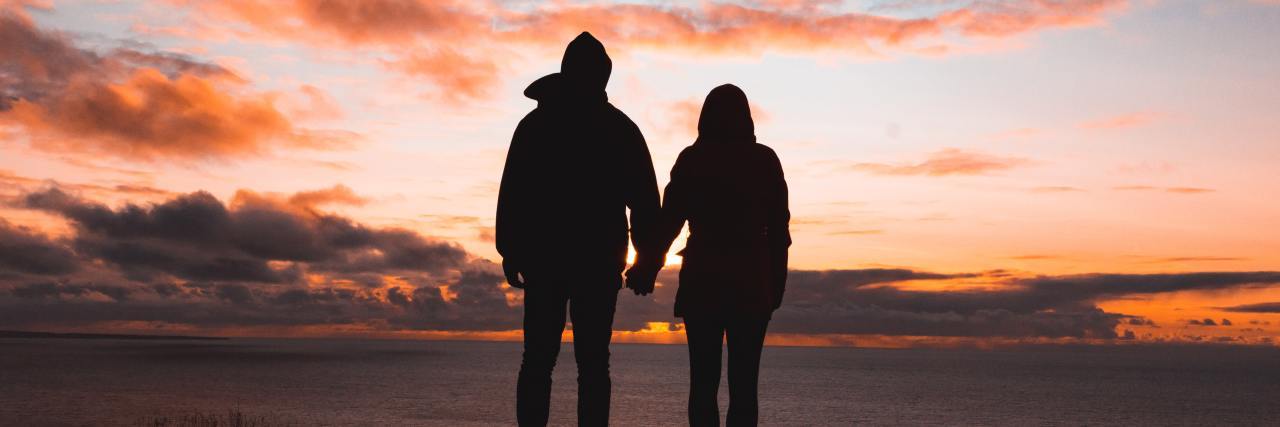 photo of silhouetted couple against sunset, holding hands on cliffside