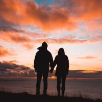 photo of silhouetted couple against sunset, holding hands on cliffside