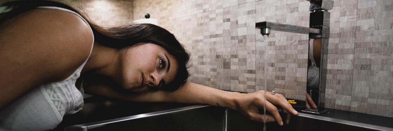 Childhood Neglect Makes Personal Hygiene Hard During COVID-19 photo of woman resting her head beside a sink with water running
